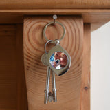 A personalised teardrop shaped keyring which is hanging on a nail on the wall. The keyring has been personalised with a photo of children. 